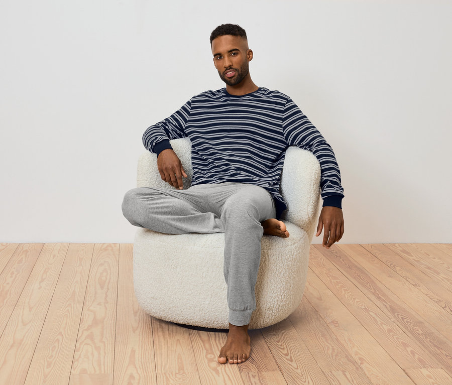 Mężczyzna siedzi w fotelu. Ma na sobie koszulkę z długim rękawem w paski i szare spodnie dresowe.