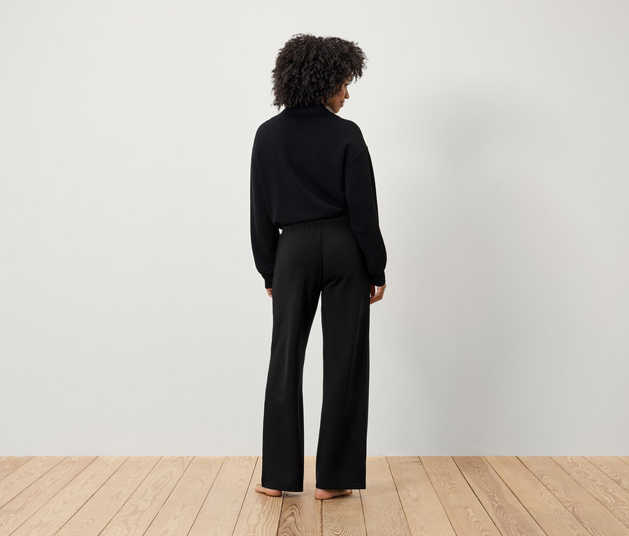 Kobieta z fryzurą afro, ubrana w czarny sweter i czarne spodnie, widziana z tyłu.