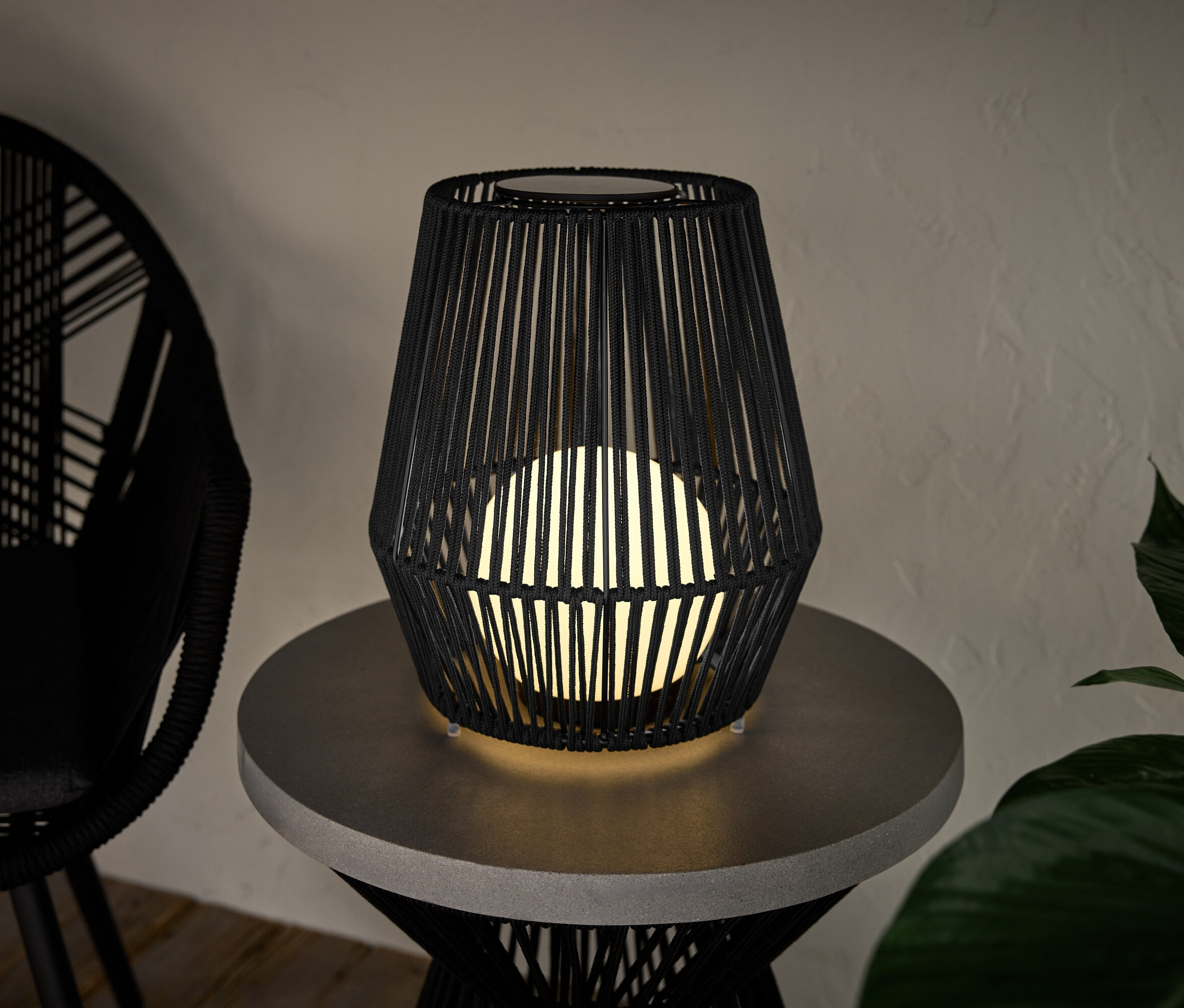 Mała latarnia solarna ze sznurkiem tekstylnym stoi na stole.