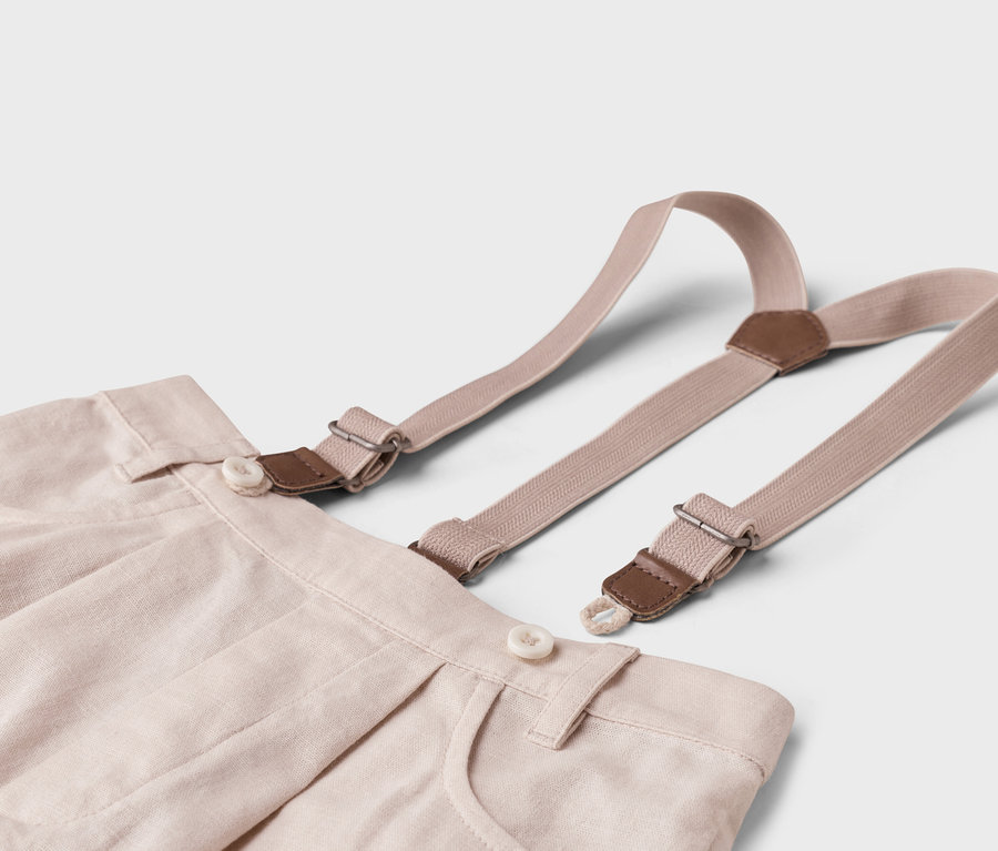 Zbliżenie beżowych spodni materiałowych ze szelkami na białym tle.