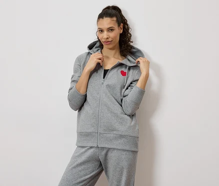 Kobieta ma na sobie szary dres z czerwonym sercem na bluzie.