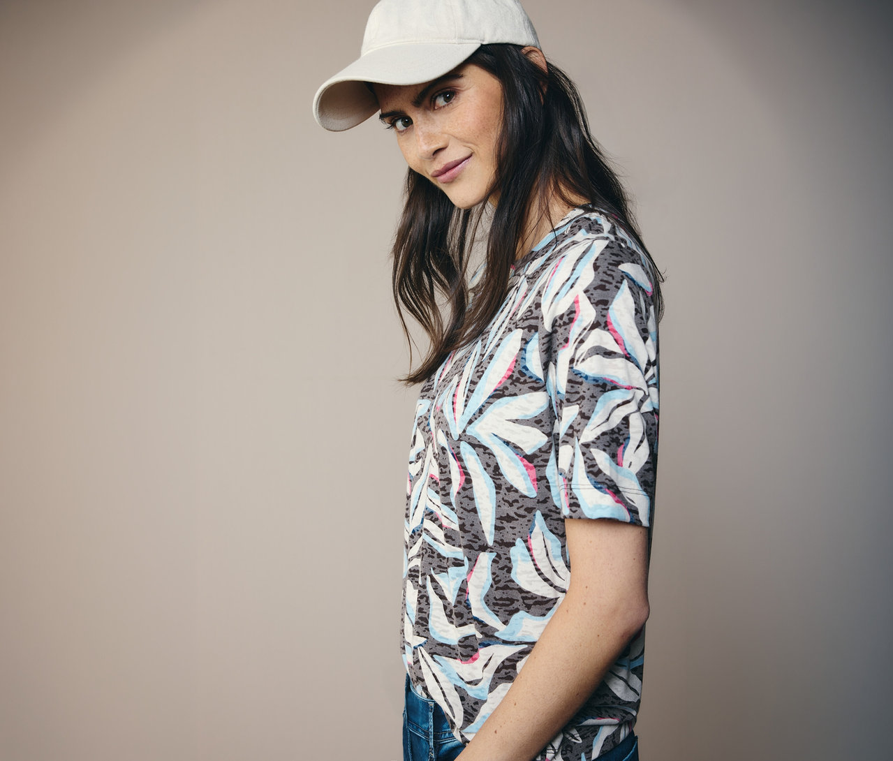 Kobieta w beżowej czapce i niebieskiej koszulce z krótkim rękawem CECIL we wzór z liśćmi.