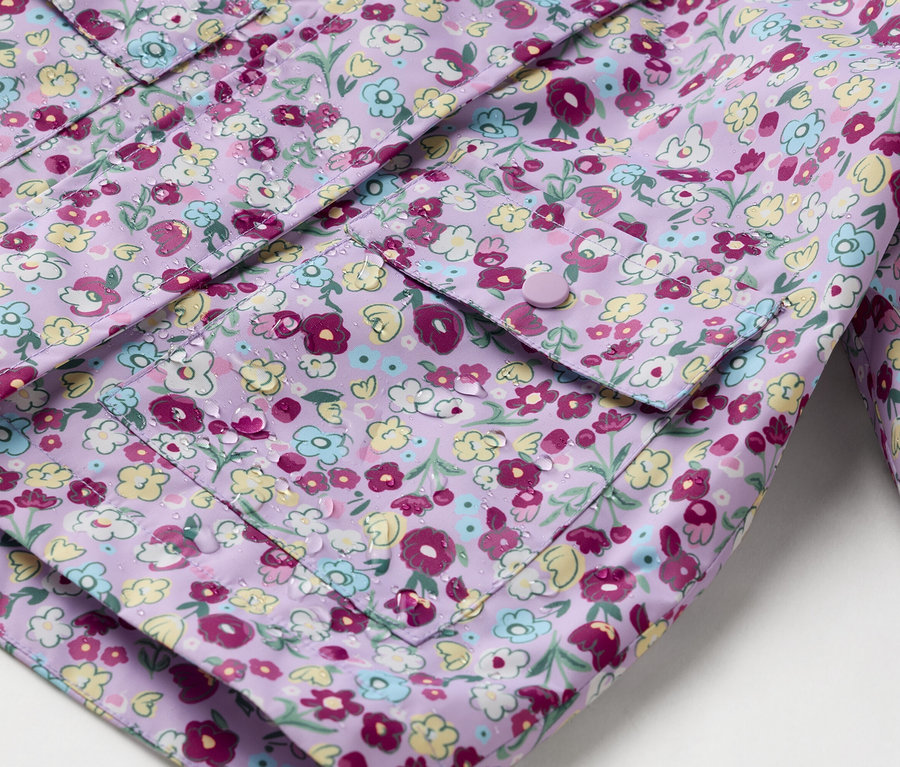 Zbliżenie fioletowej kurtki przeciwdeszczowej w kwiaty z naszytymi kieszeniami zapinanymi na guziki.