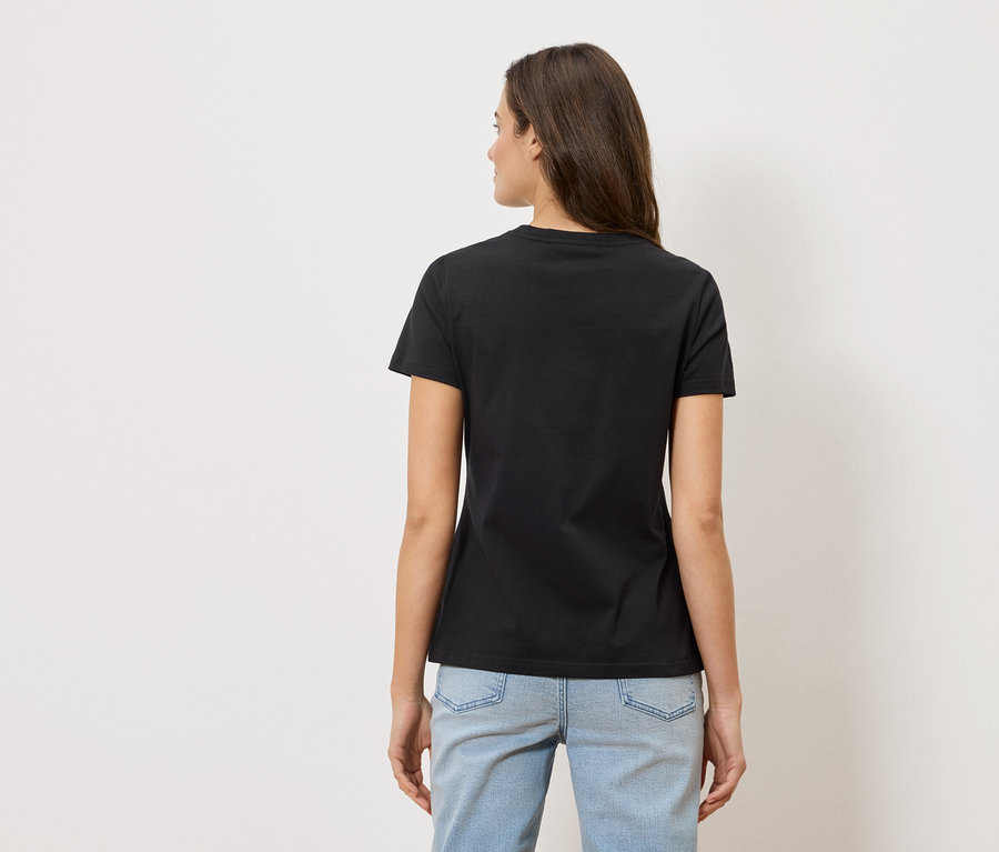 Widok z tyłu kobiety z długimi brązowymi włosami, ubranej w czarny T-shirt i jasnoniebieskie dżinsy.