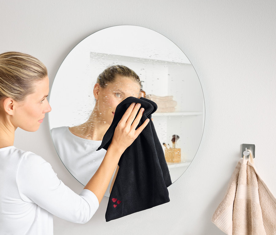 Kobieta czyści zaparowane okrągłe lustro czarną ściereczką.