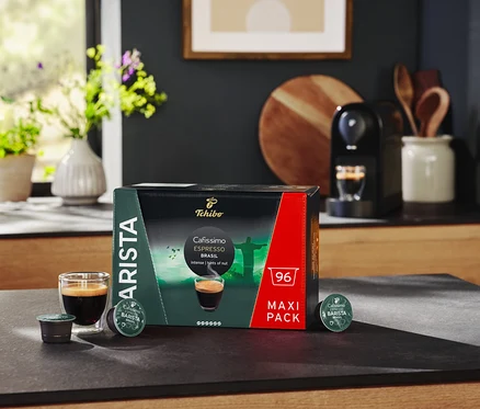 Na stole stoi opakowanie kapsułek Cafissimo BARISTA Espresso Brasil, szklanka espresso i ekspres do kawy.