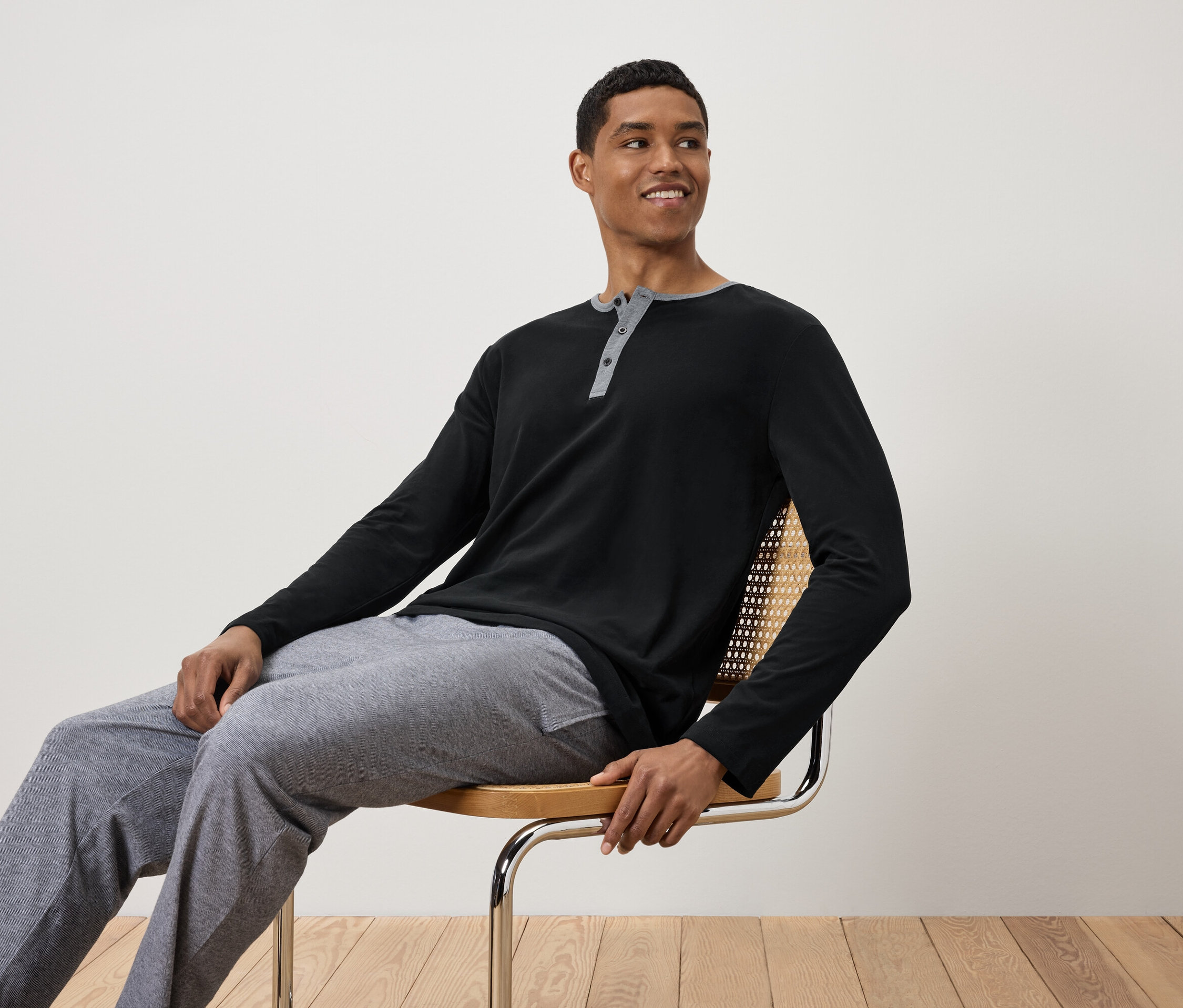 Mężczyzna siedzi na krześle, ubrany w czarną koszulkę z długim rękawem i szare spodnie dresowe.