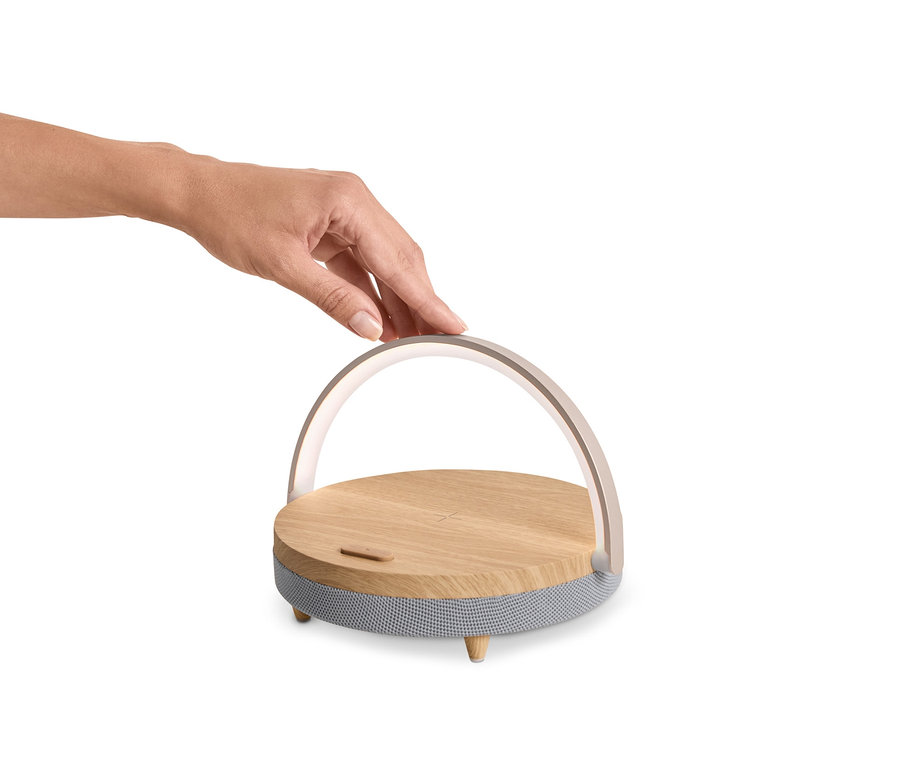 Ręka dotyka głośnika Bluetooth z bezprzewodową ładowarką i lampką LED.