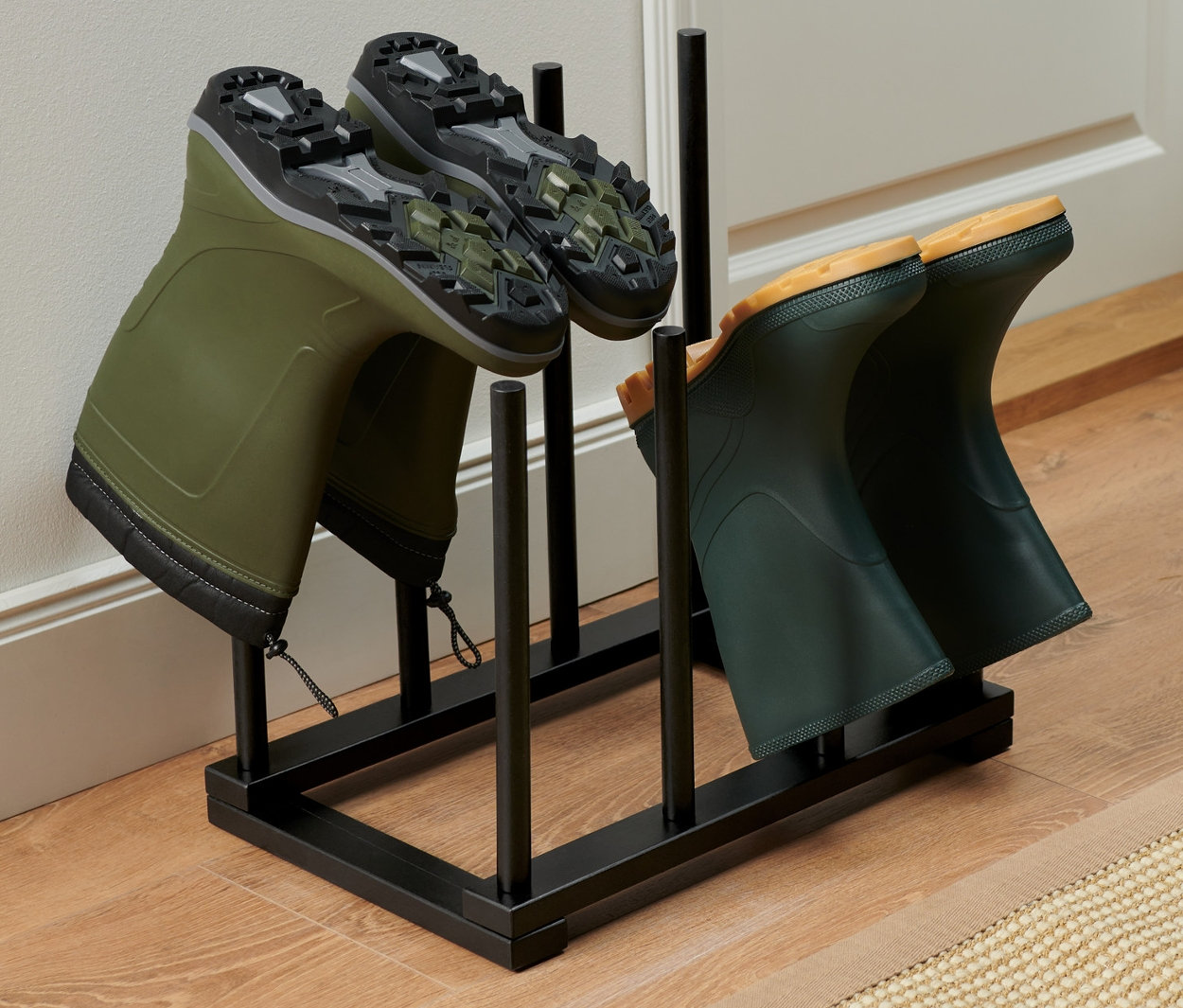 Dwie pary zielonych kaloszy stoją na czarnym stojaku na buty.