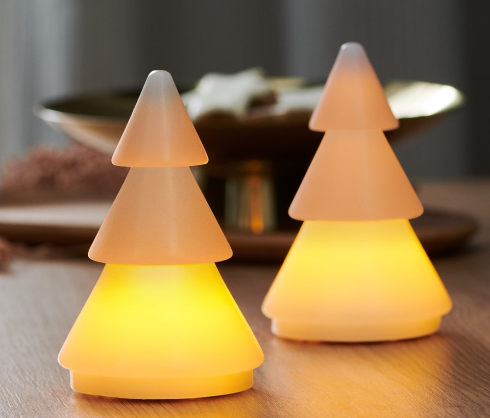 Dwie choinki LED z prawdziwego wosku stoją na drewnianym stole. W tle widoczne okno.