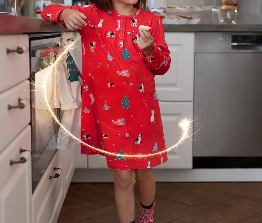 Dziewczynka w czerwonej koszuli nocnej w świąteczne wzory je ciastko i trzyma zimny ogień. Ma na sobie Skarpetki, 5 par.