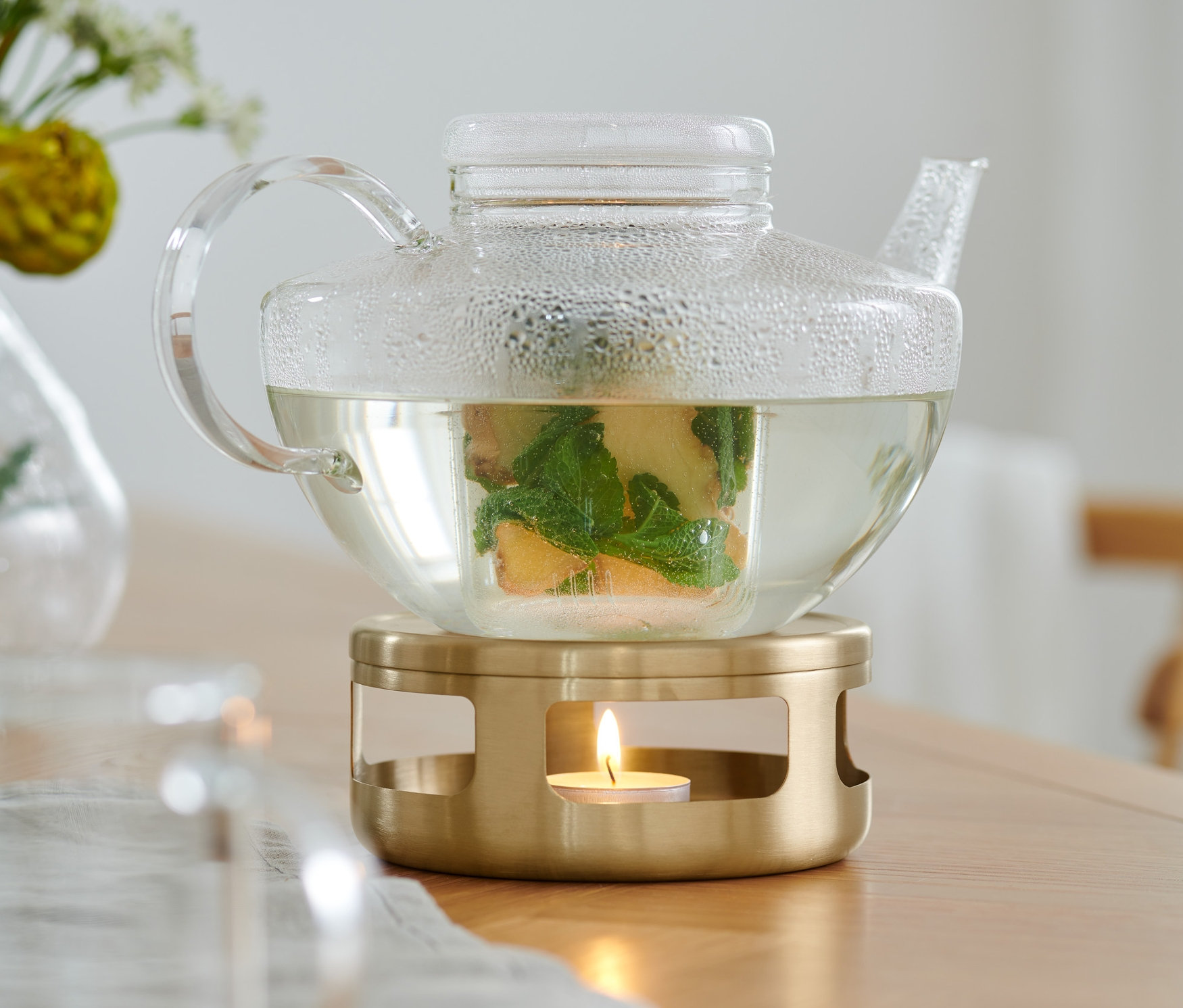 Przezroczysty szklany czajnik z herbatą stoi na złotym podgrzewaczu.
