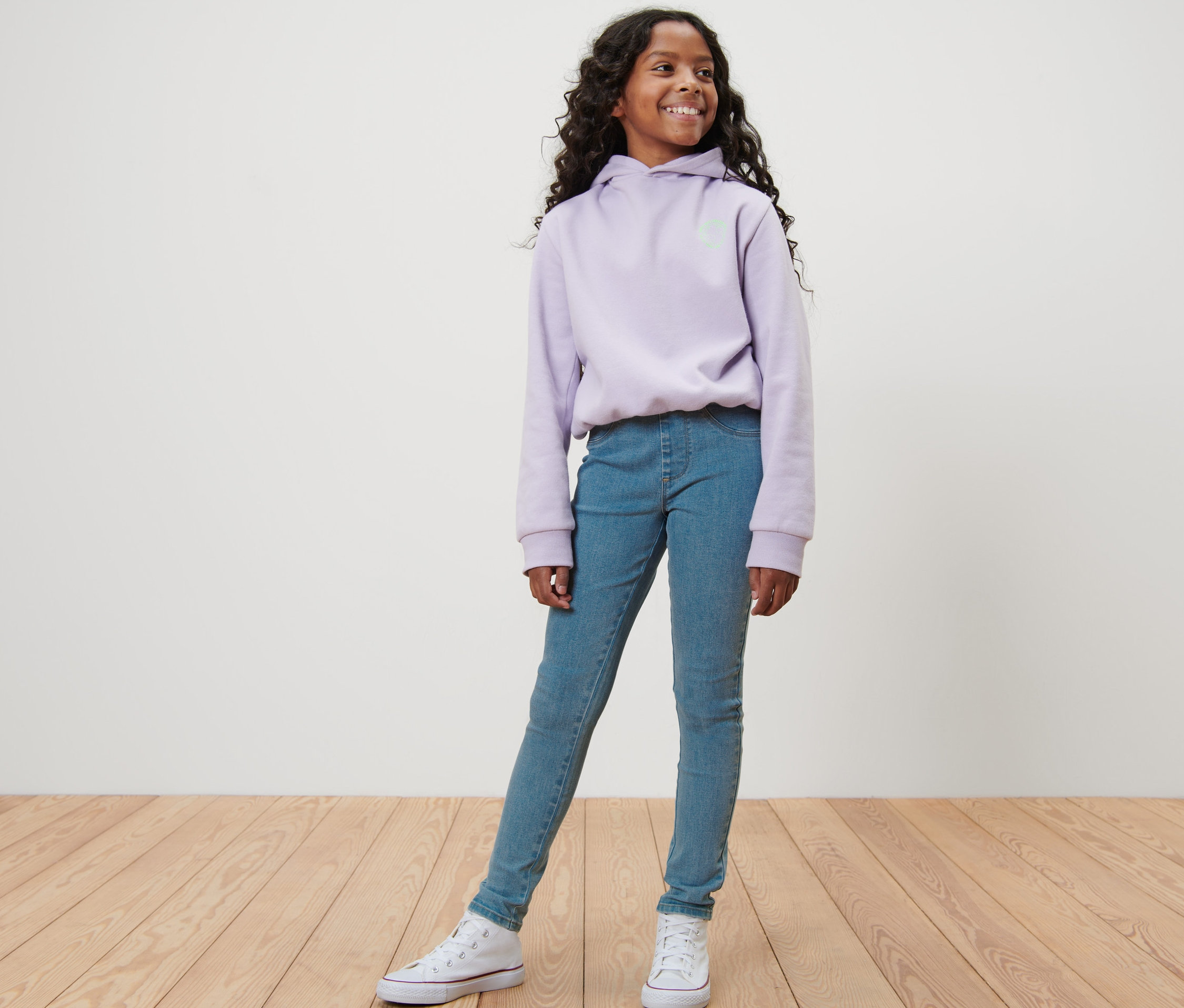 Dziewczyna pozuje w niebieskich tregginsach dziecięcych – fason „Jule” i fioletowej bluzie z kapturem.