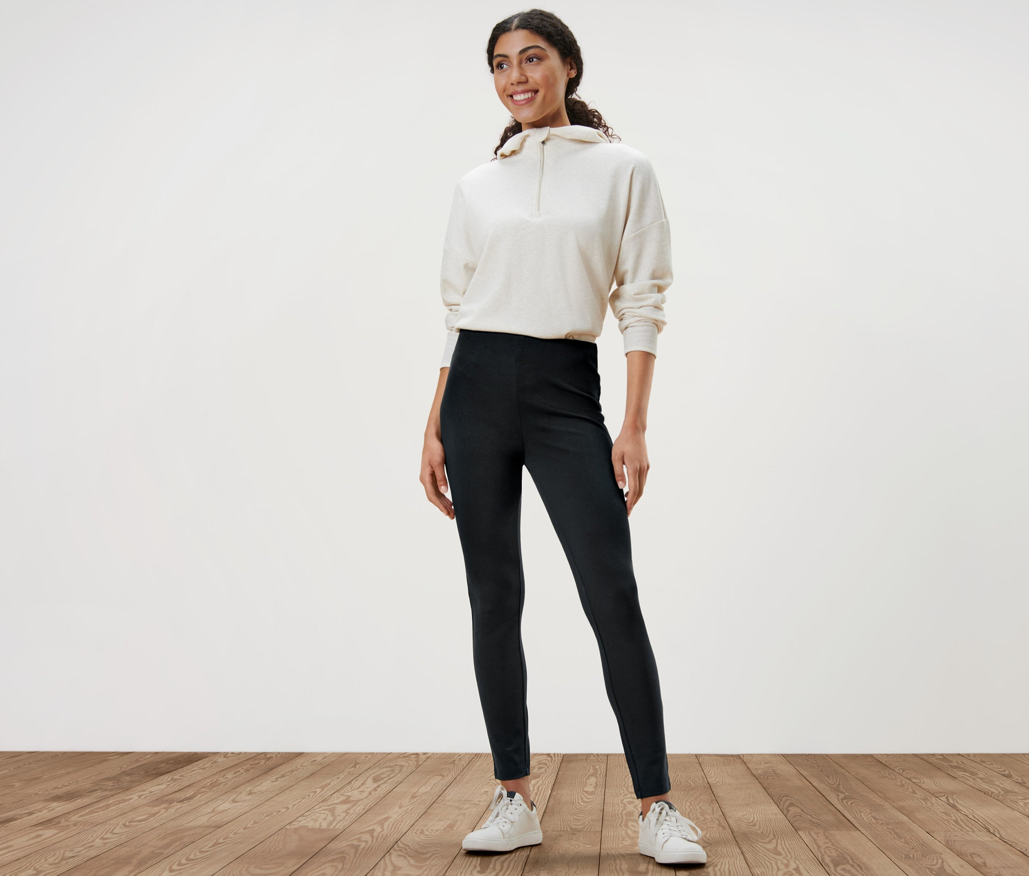 Kobieta stoi w grubych legginsach, białej bluzie i białych tenisówkach.