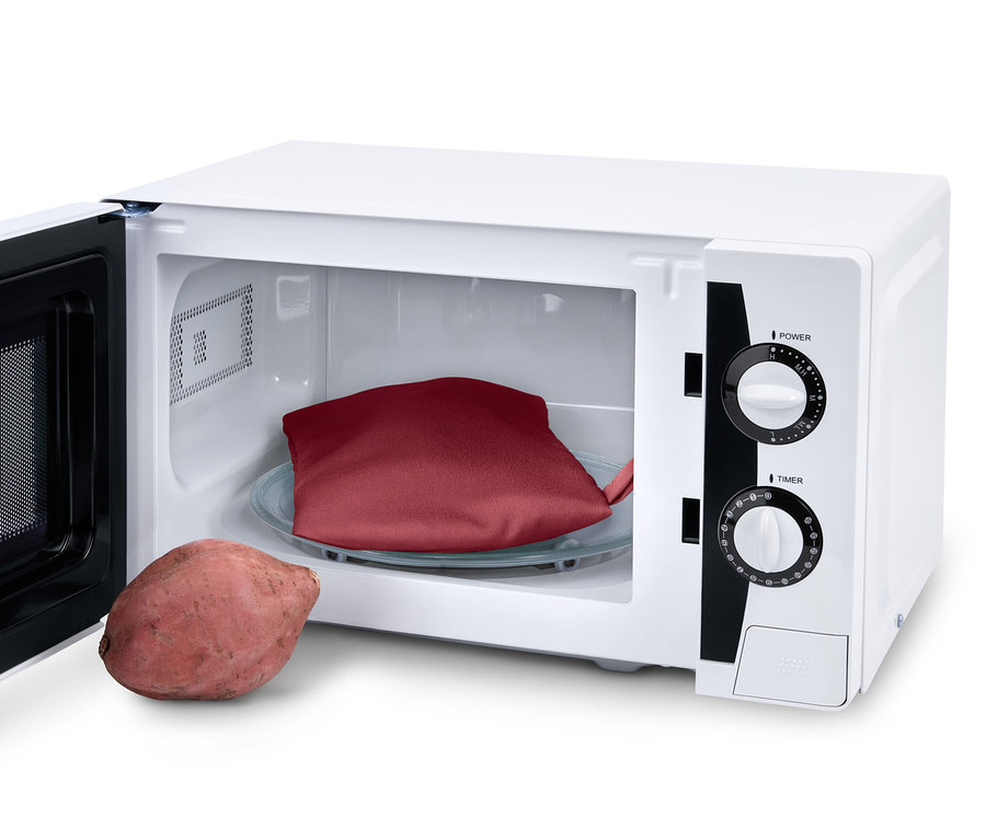 Czerwona torba do gotowania ziemniaków w kuchence mikrofalowej leży na szklanym talerzu wewnątrz kuchenki mikrofalowej, obok leży ziemniak.