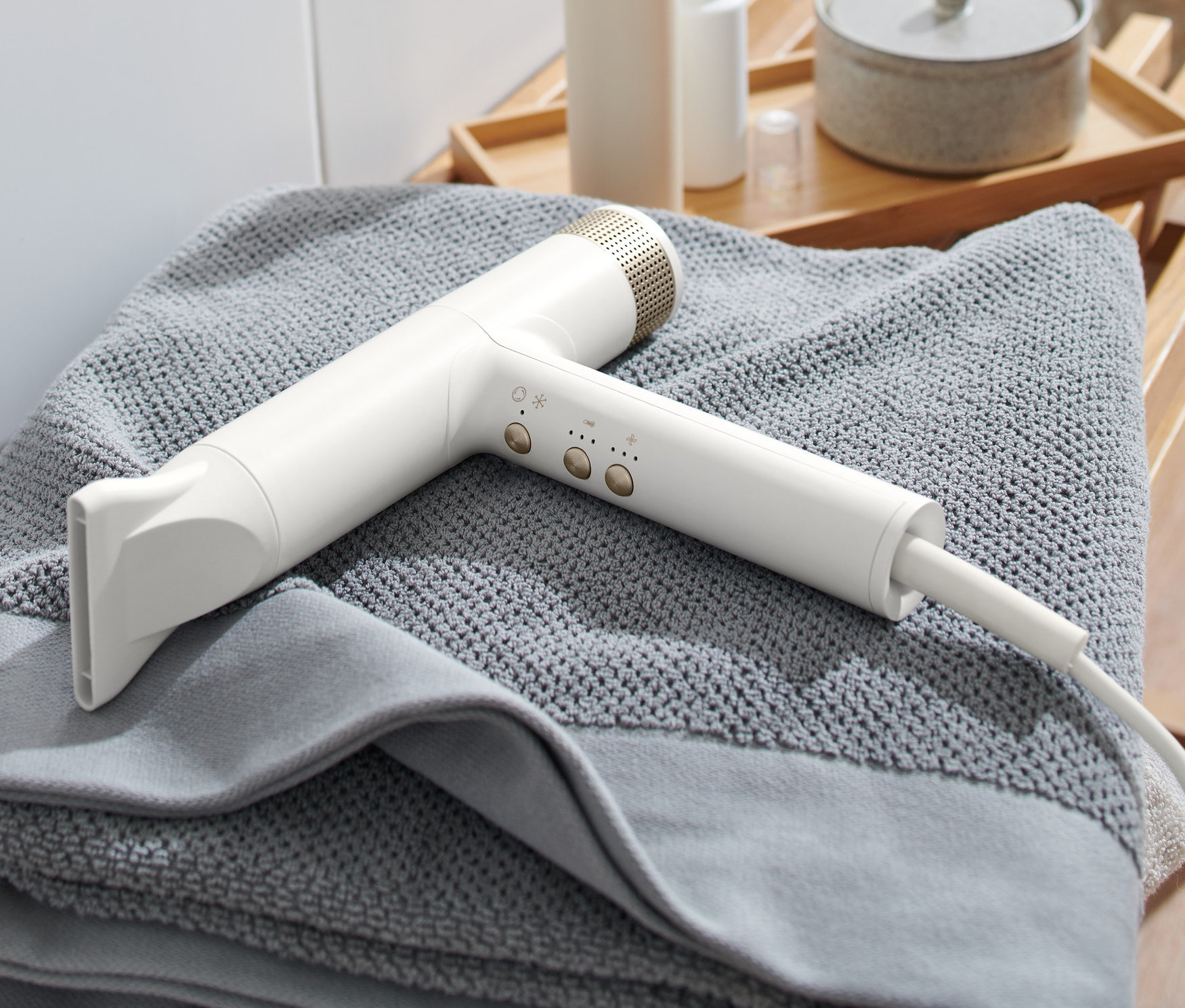 Biała suszarka do włosów premium leży na szarym ręczniku na drewnianym stołku.