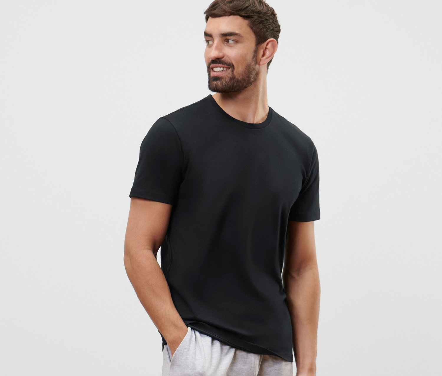 Mężczyzna z brodą ma na sobie czarną koszulkę z okrągłym dekoltem z 2-częściowego zestawu i szare szorty.