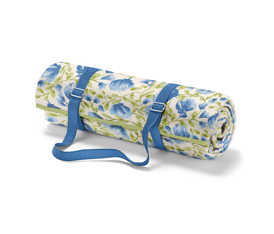 Zrolowany mały koc piknikowy z niebieskimi kwiatami i zielonymi łodygami, zabezpieczony niebieskimi paskami.