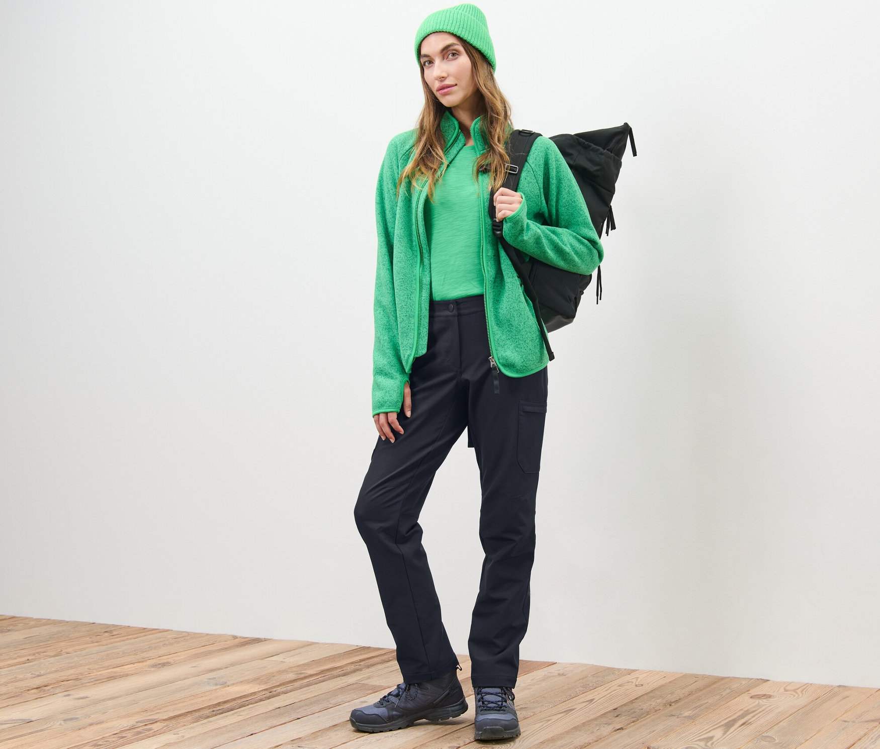 Kobieta pozuje w zielonym swetrze, czapce i czarnych spodniach cargo z softshellu.