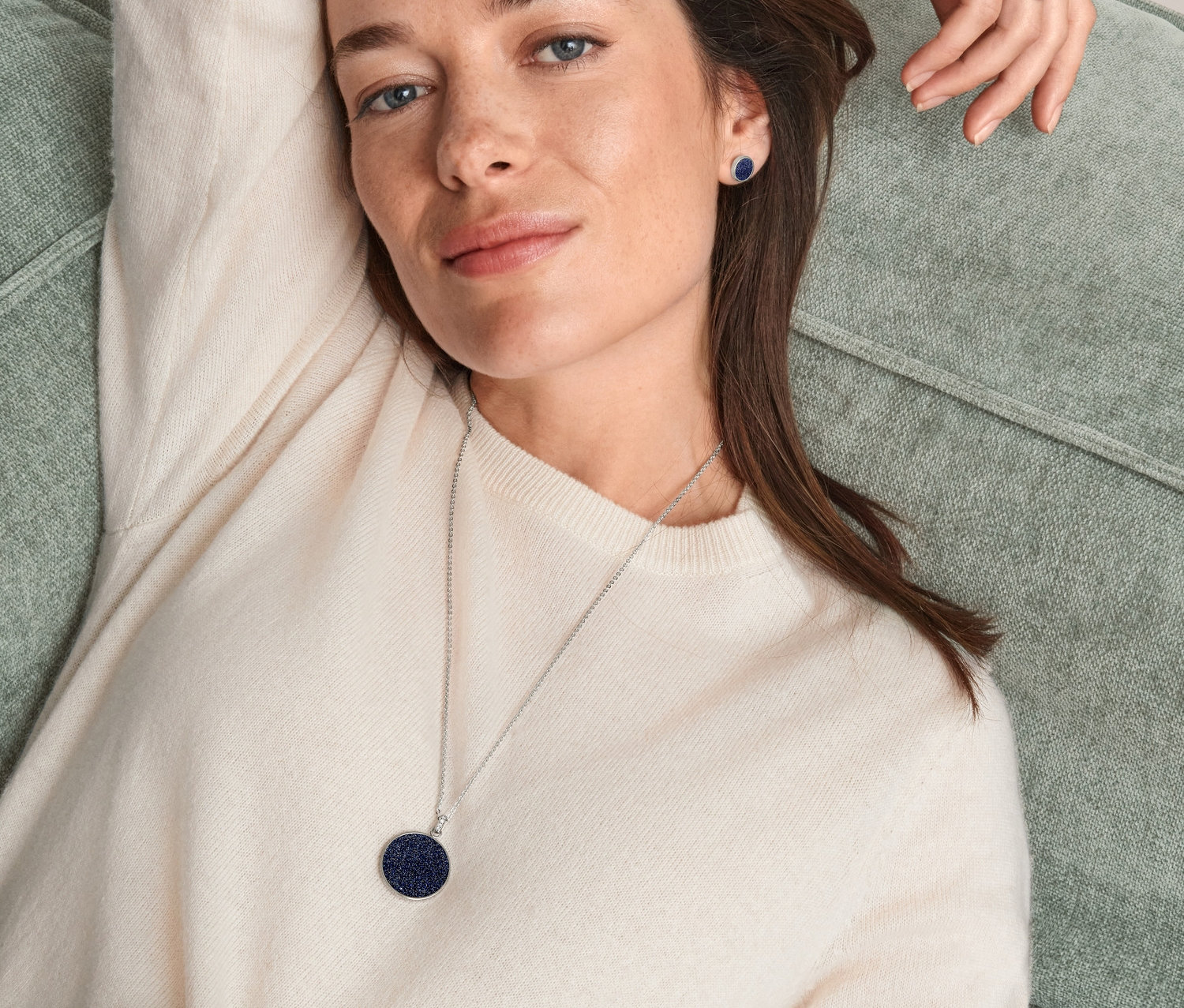 Kobieta leży na kanapie i ma na sobie pierścionek, kolczyki na sztyft i naszyjnik »Rozgwieżdżone niebo«.