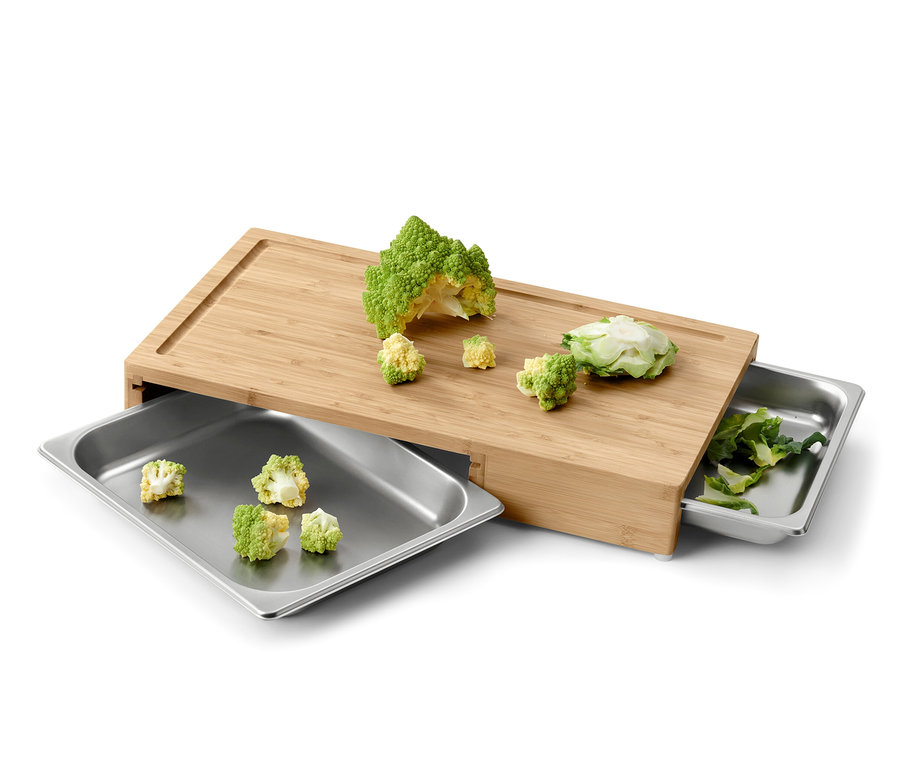 Deska do krojenia z pokrojonymi warzywami i dwiema metalowymi tackami.