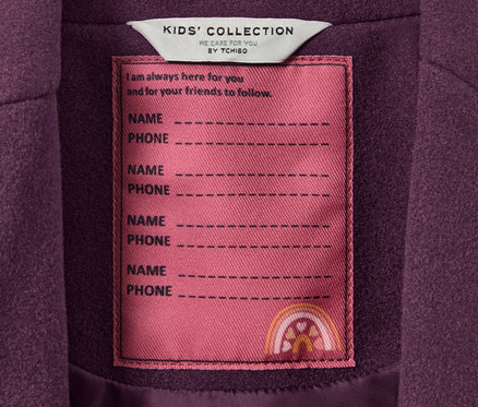 Zbliżenie na płaszcz dziecięcy z metką KIDS' COLLECTION z miejscem na imię i numer telefonu.