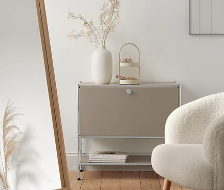 Wnętrze z beżową metalową szafką typu sideboard „CN3” z klapą, lustrem stojącym z bambusową ramą i fotelem z tkaniny bouclé z drewnianymi nogami.