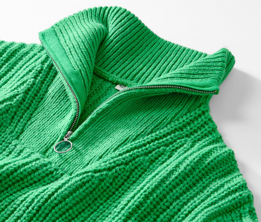 Zbliżenie na zielony sweter o grubym splocie z kołnierzem typu troyer i rozpiętym zamkiem błyskawicznym.