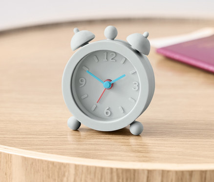 Szary budzik podróżny stoi na drewnianym stoliku obok paszportu.