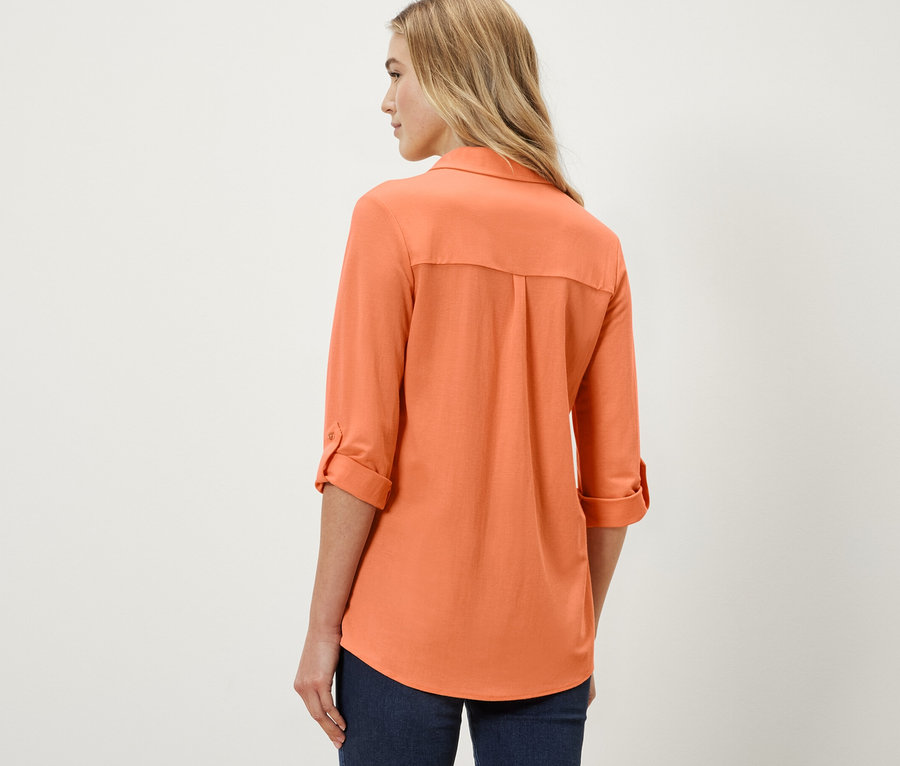 Kobieta ma na sobie brzoskwiniową bluzkę z dżerseju piqué.