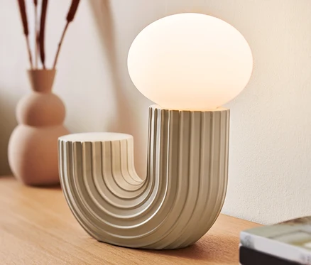 Designerska lampka stołowa LED stoi na drewnianym stole obok wazonu i książek.