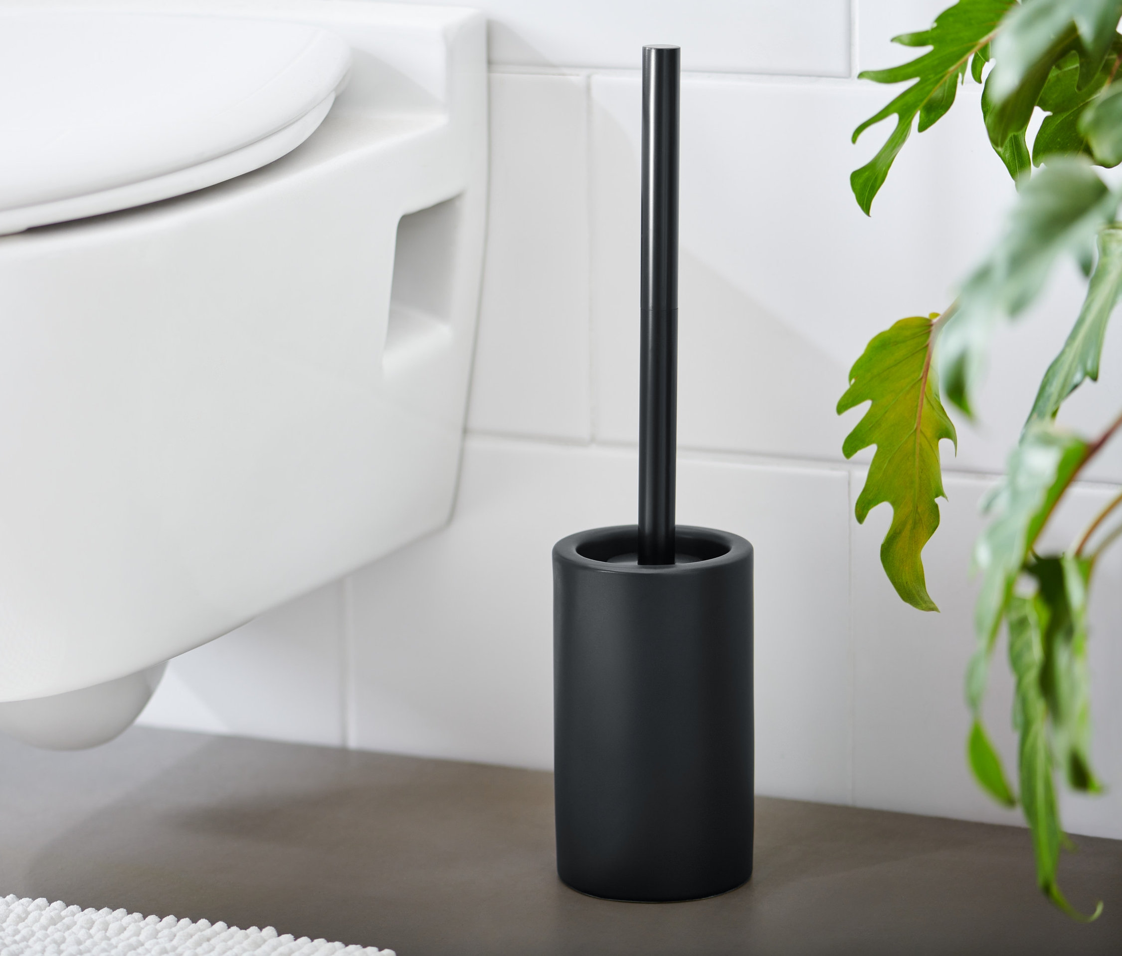 Czarna szczotka do WC stoi obok białej toalety.