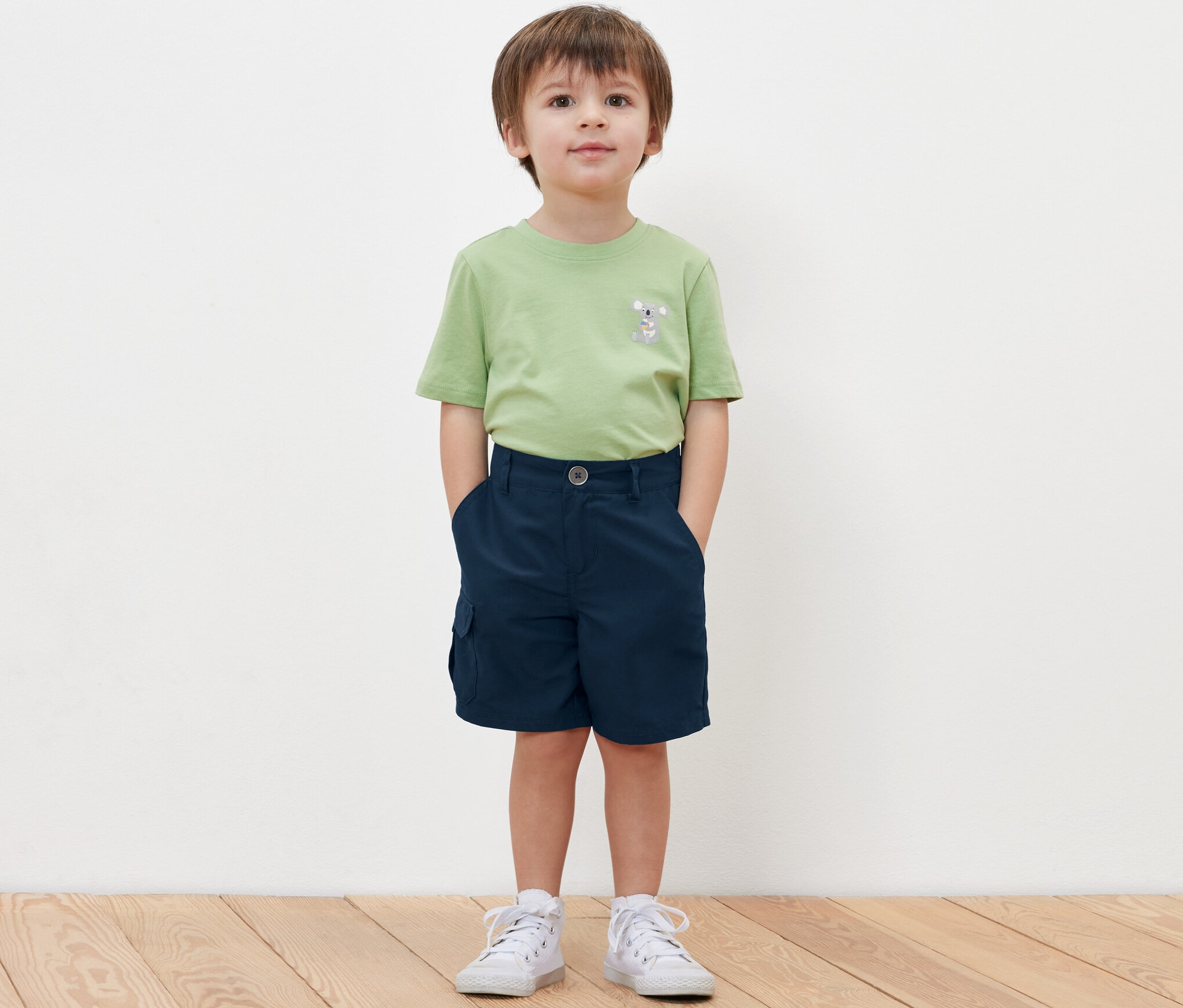 Chłopiec stoi z rękami w kieszeniach szortów funkcyjnych.
