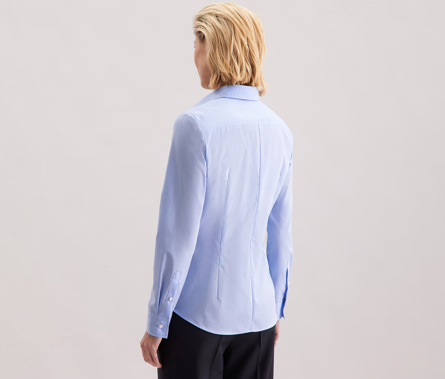 Zdjęcie z tyłu kobiety z blond włosami do ramion, ubranej w jasnoniebieską bluzkę Seidensticker Slim Fit non iron.