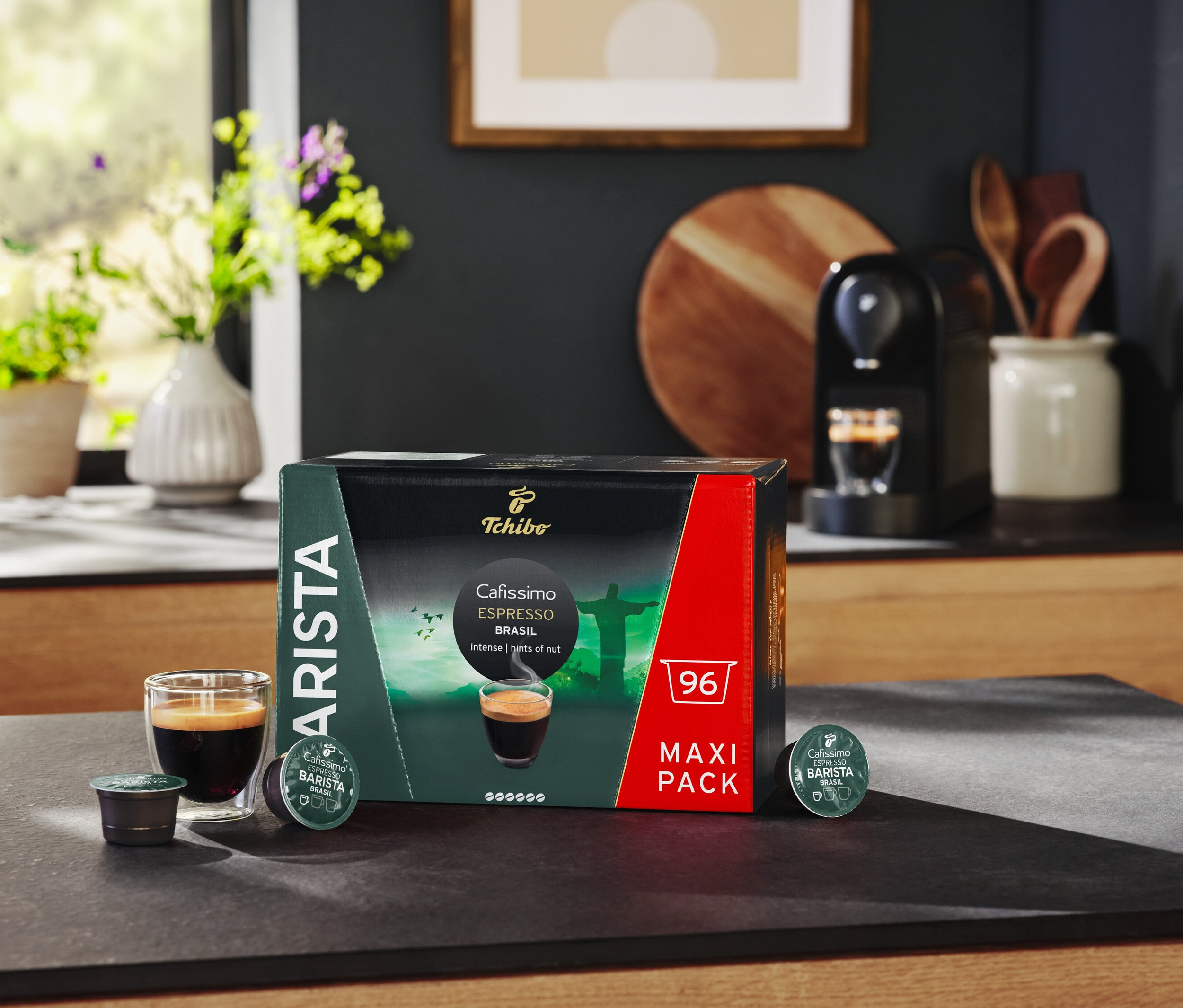 Na stole stoi opakowanie kapsułek Cafissimo BARISTA Espresso Brasil, szklanka espresso i ekspres do kawy.