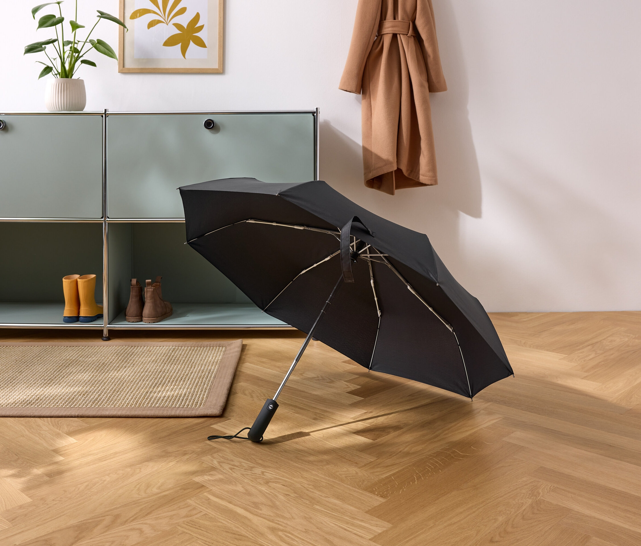 Czarny parasol leży na parkiecie w przedpokoju.