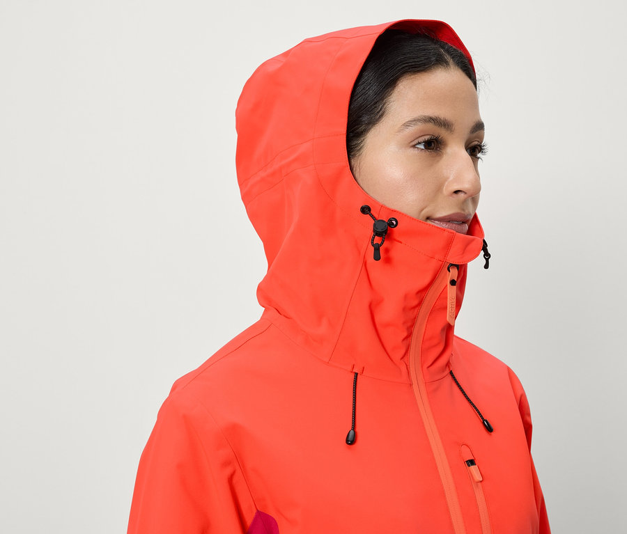 Kobieta ma na sobie koralową kurtkę z kapturem.