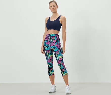 Kobieta ma na sobie biustonosz sportowy i legginsy sportowe o długości 3/4, wzór na całej powierzchni.
