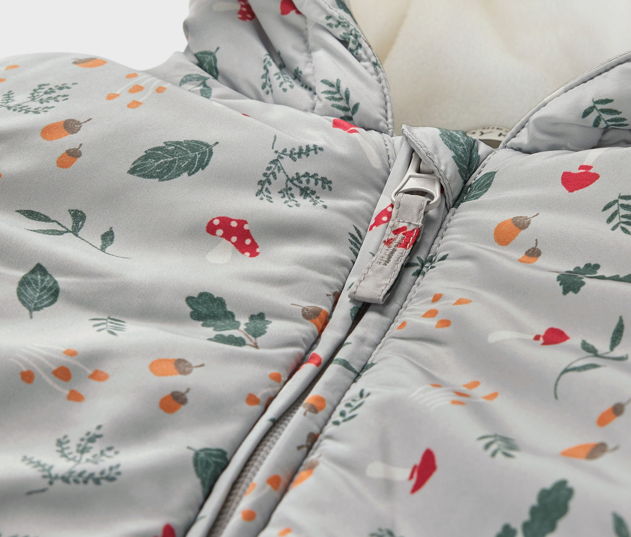 Szczegółowy widok niemowlęcego kombinezonu zimowego we wzór z liści, grzybów i żołędzi.