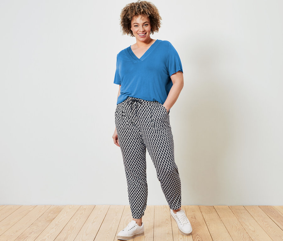 Kobieta pozuje w kobaltowej koszulce i wzorzystych spodniach z dżerseju.
