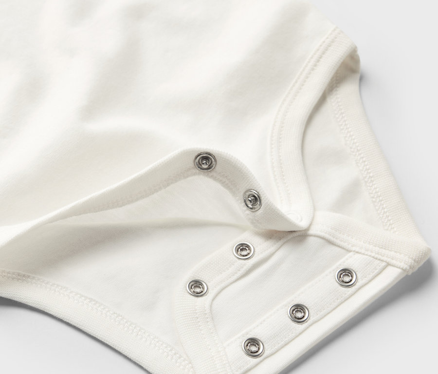 Zbliżenie na białe body rosnące z dzieckiem, zapinane na zatrzaski.