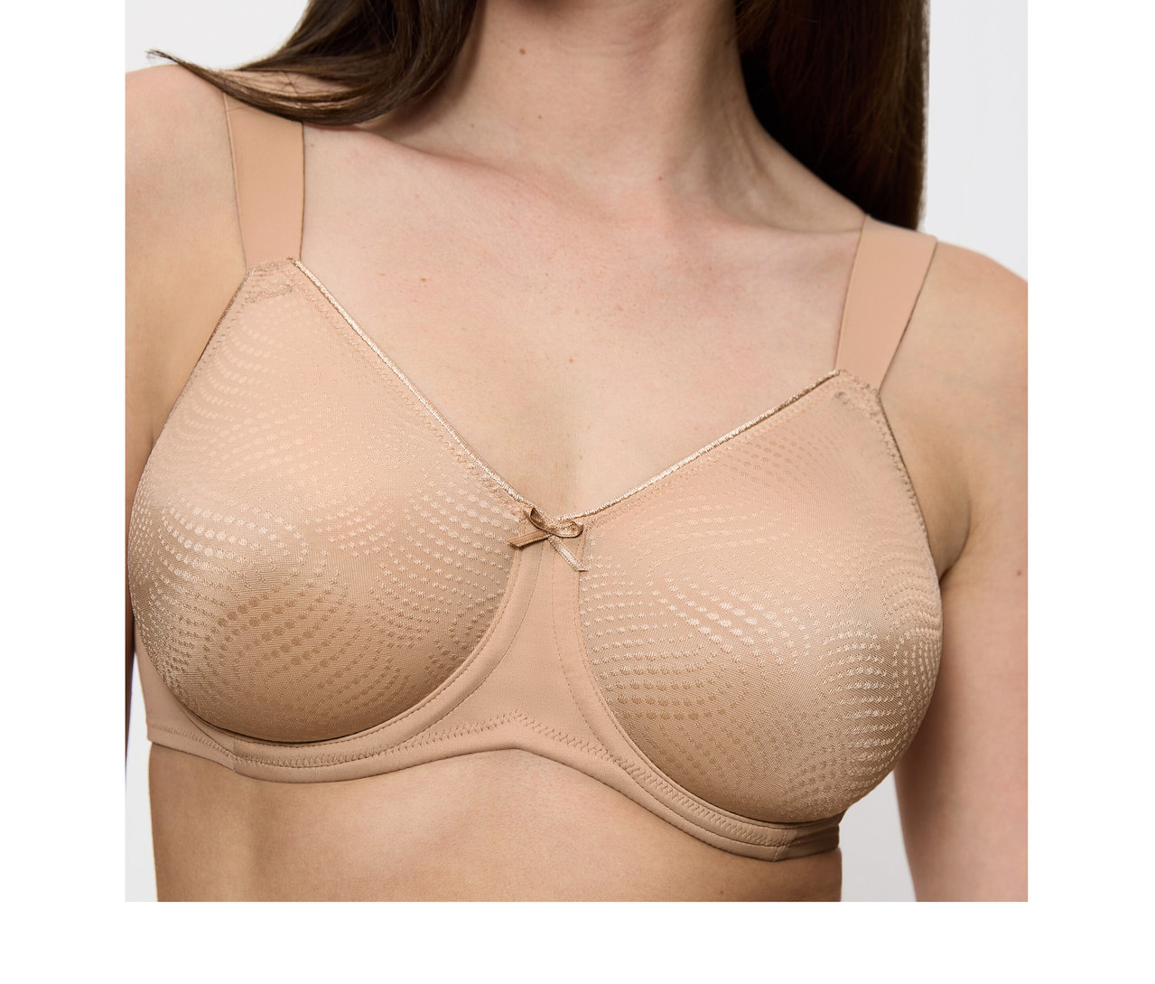 Kobieta nosi biustonosz Triumph Essential Minimizer W X w kolorze cielistym, z szerokimi ramiączkami, teksturowanymi miseczkami i małą kokardką.
