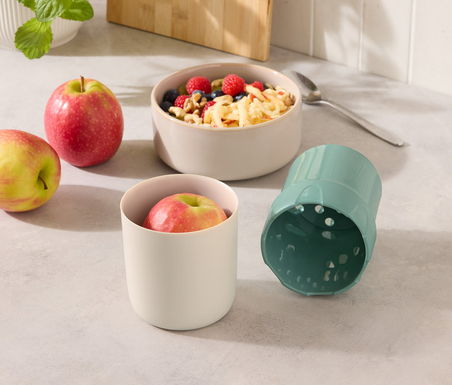 Dwa jabłka obok miski z musli i kubka z jabłkiem i niebieskiego kubka.