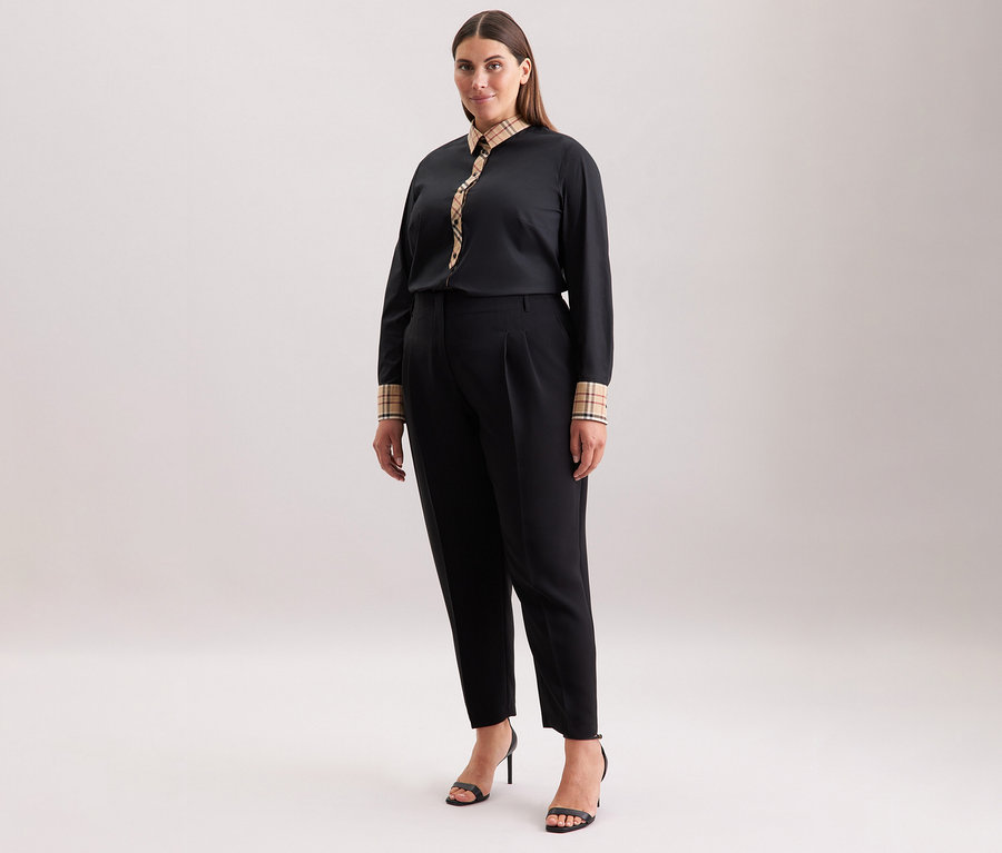 Kobieta ma na sobie czarne spodnie i popelinową bluzkę Seidensticker w kratę oraz czarne buty na wysokim obcasie.