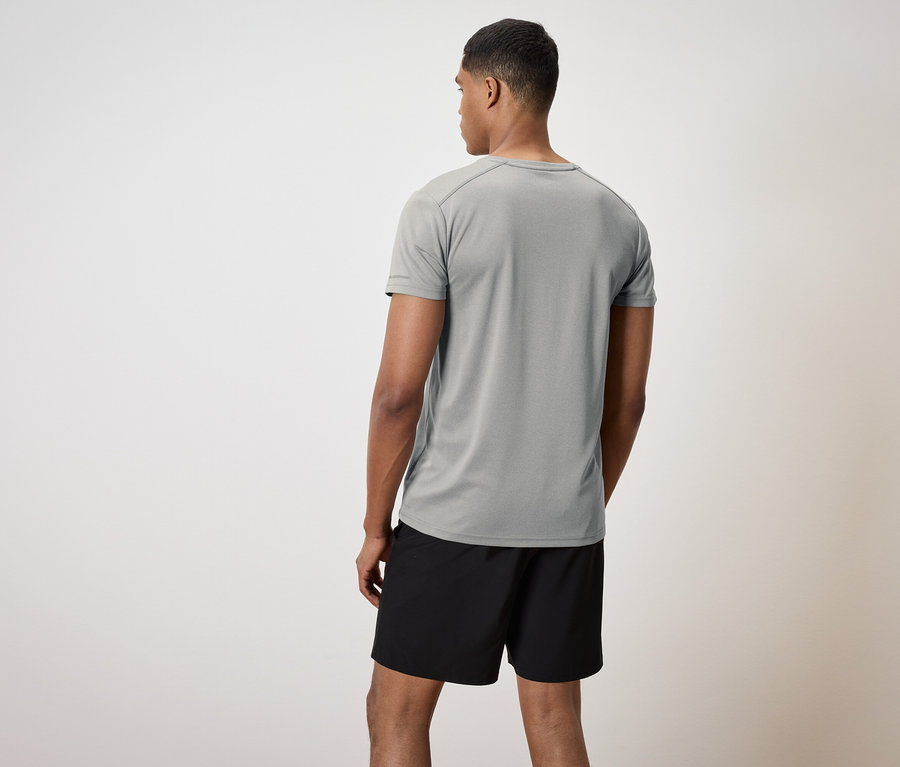Mężczyzna tyłem do kamery ma na sobie szarą koszulkę i czarne szorty.