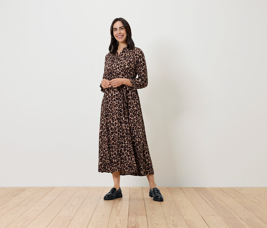 Kobieta pozuje w wzorzystej sukience z długim rękawem i czarnych butach.