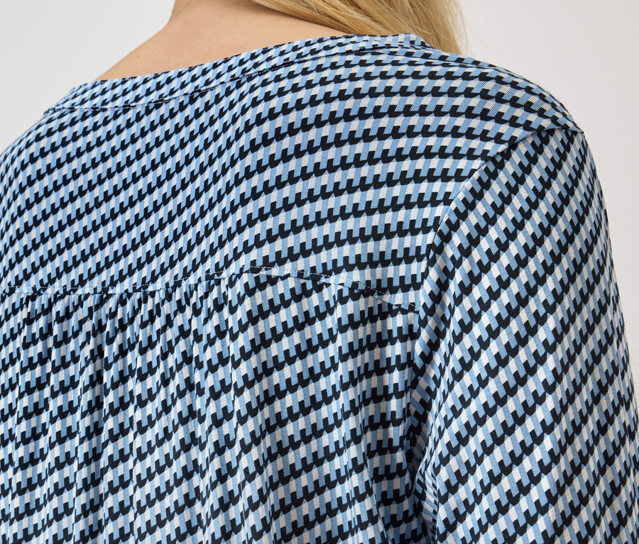 Widok z tyłu kobiety z blond włosami w niebiesko-białej bluzce w pepitkę.