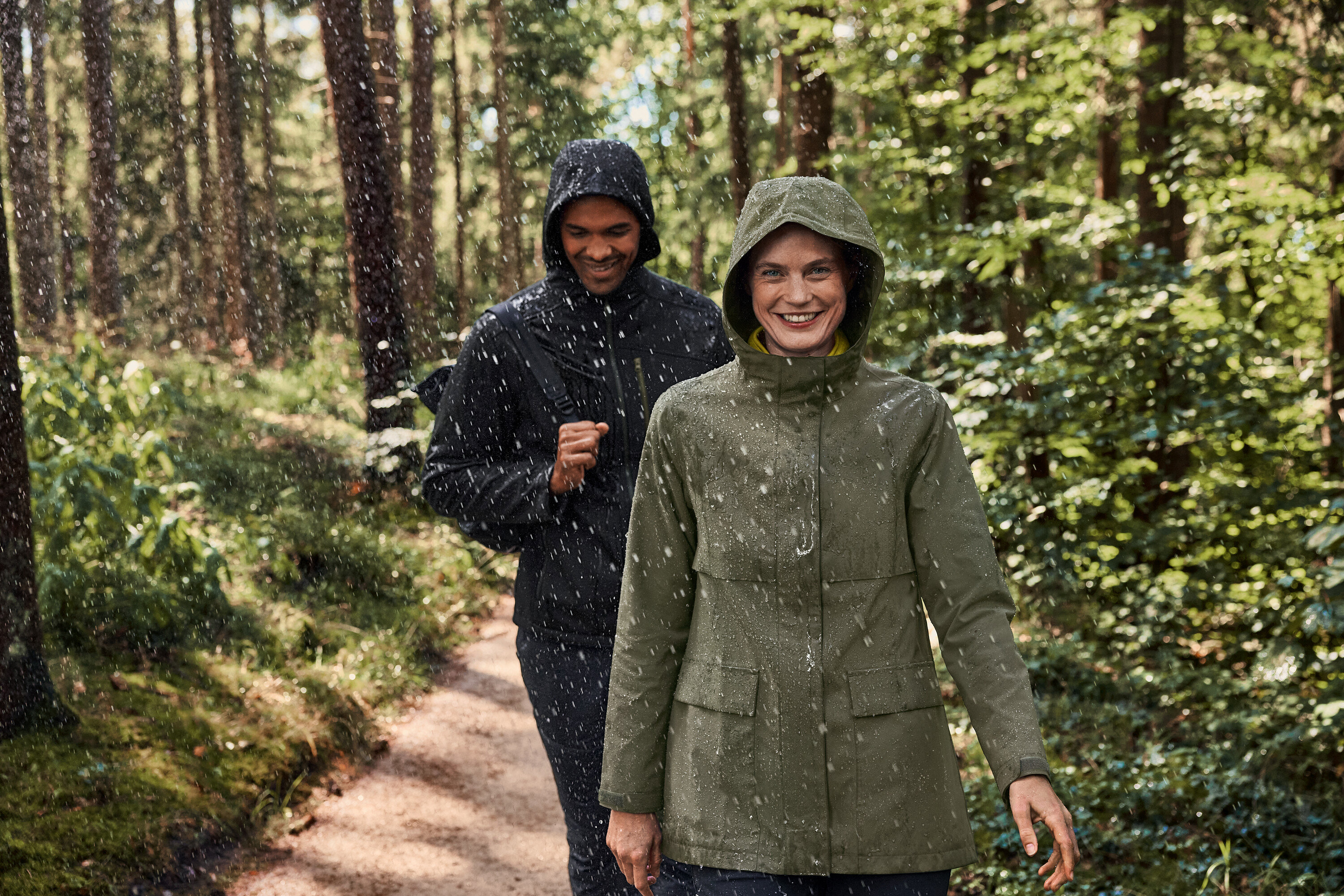 Dwie osoby idą w deszczu przez las. Kobieta ma na sobie bluzę polarową z rozpinanym golfem khaki-antracyt.