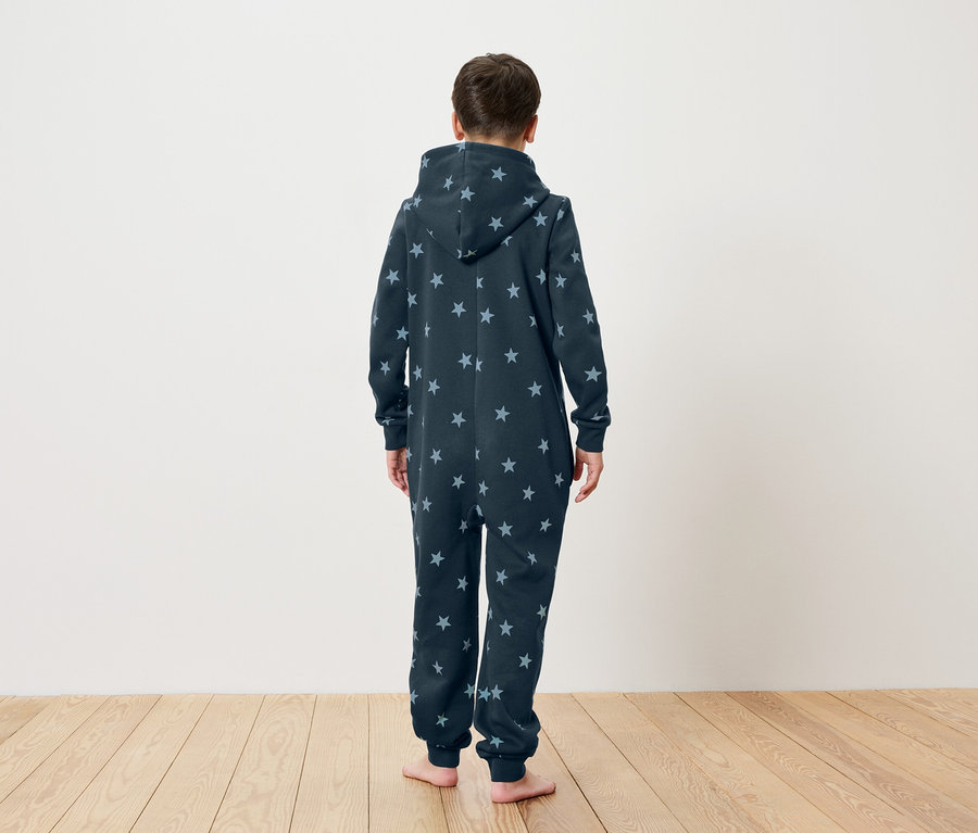 Dziecko stoi tyłem do kamery, ubrane w granatowy kombinezon w gwiazdki z kapturem.