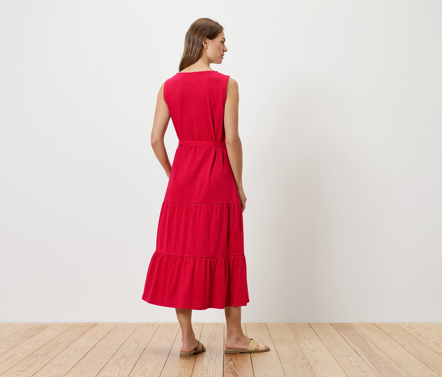 Kobieta od tyłu w czerwonej sukience midi bez rękawów z paskiem i płaskimi sandałami.